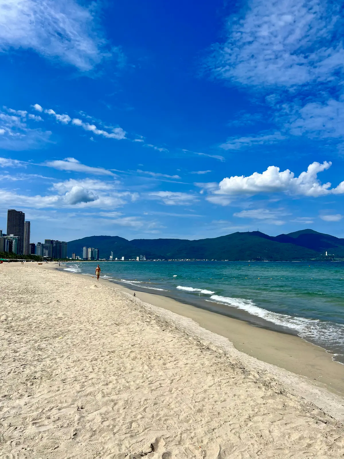 Mỹ Khê beach under a hot blue sky, pale sand curving toward the city and the Sơn Trà mountains