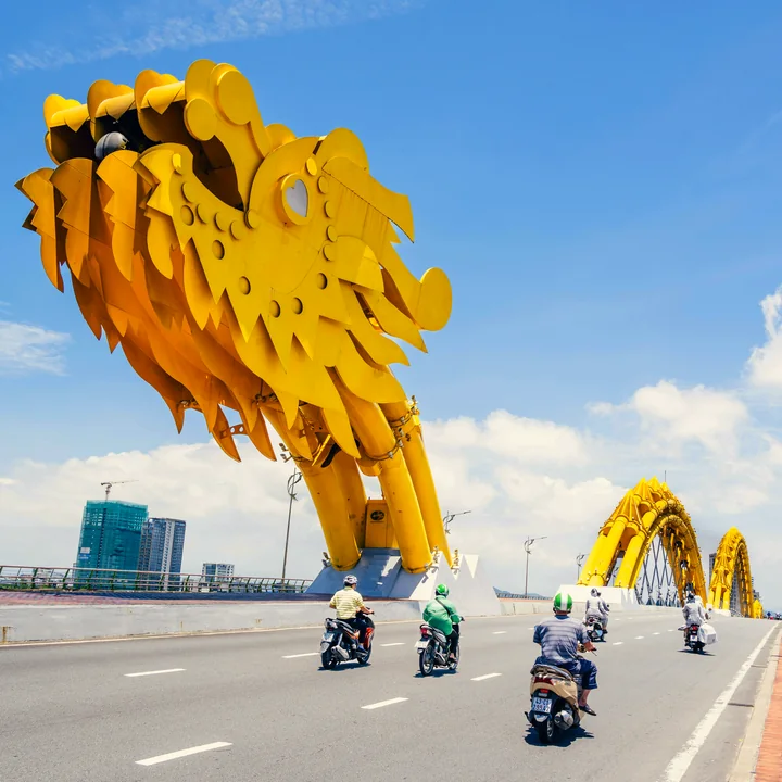 The finished puzzle: the golden Dragon Bridge head over a Đà Nẵng road at midday, motorbikes crossing