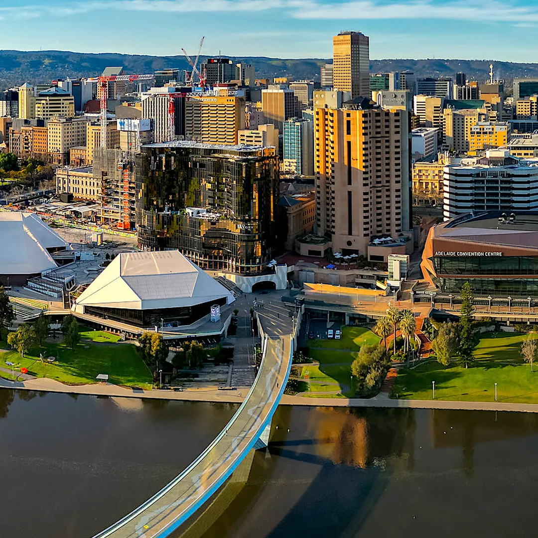 Adelaide from above the River Torrens: the curved Riverbank Footbridge, the Festival Centre's white roofs and the city towers, with the hills behind