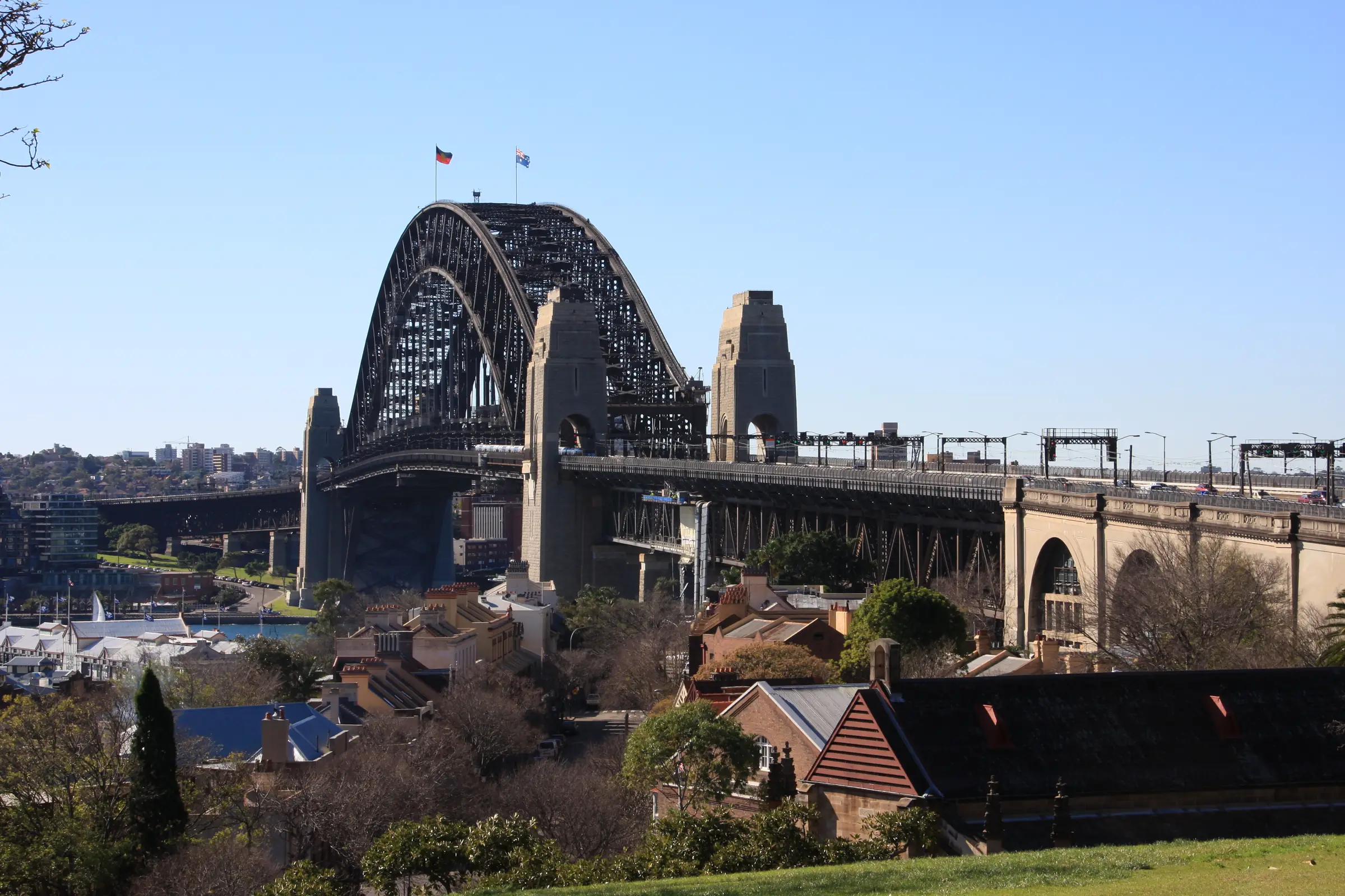 Sydney Harbour Bridge rising beyond The Rocks rooftops from Observatory Hill in sunshine