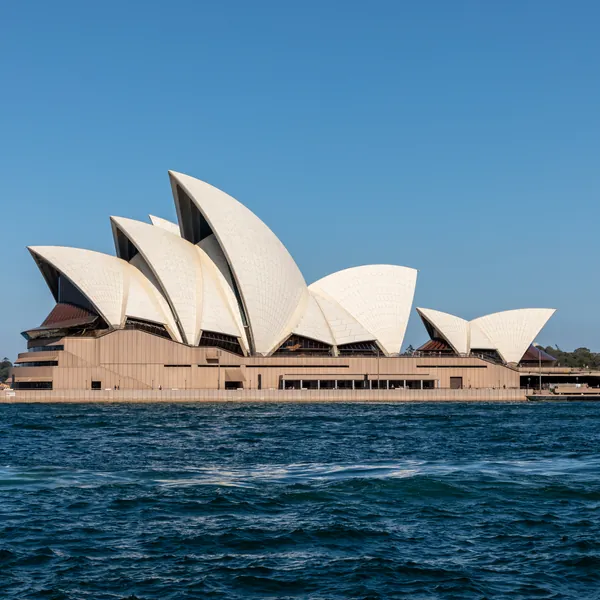Sunlit white Opera House shells against a clear blue sky above the harbour